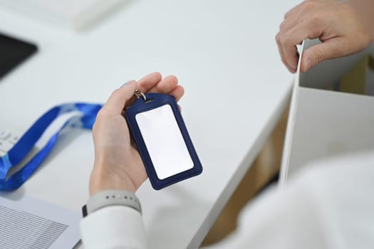 Close up shot of male employee holding blank ID card badge sitting at office desk.