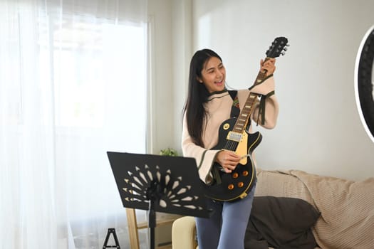 Young female musician playing electric guitar while recording a video for her social media channel.