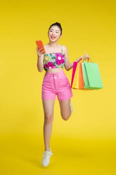 Young energetic Asian woman holding blank use smartphone searching shop retail with colorful shopping bags 