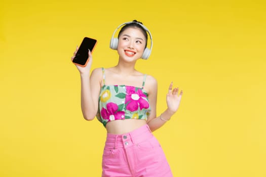 Young Asian woman wearing headphones dancing and listening to music from smartphone