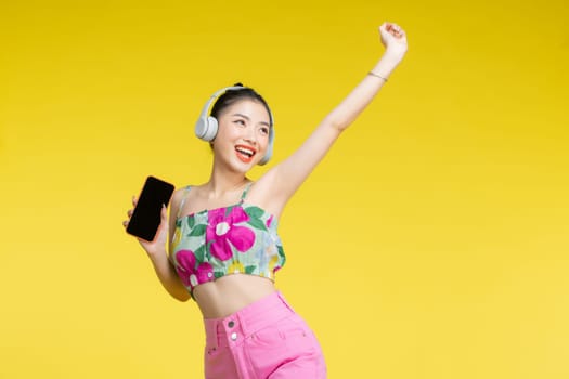 Happy cheerful Asian woman wearing wireless headphones listening to music from smartphone