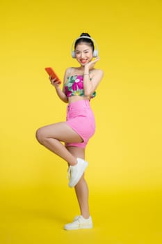 Happy smiling young Asian woman listening to music from headphones isolated on yellow background