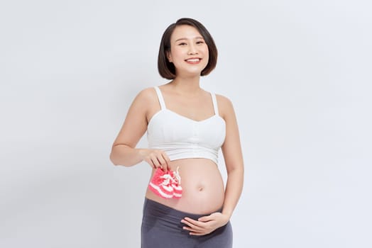 Young asian woman isolated on white background pregnant and holding baby booties