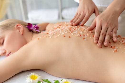 Closeup woman customer having exfoliation treatment in luxury spa salon with warmth candle light ambient. Salt scrub beauty treatment in health spa body scrub. Quiescent