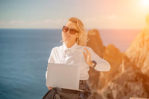 Business woman on nature in white shirt and black skirt. She works with an iPad in the open air with a beautiful view of the sea. The concept of remote work