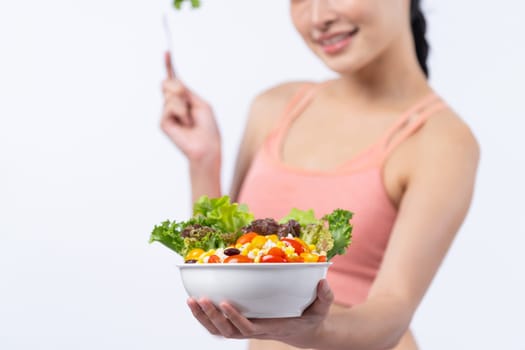 Young sporty Asian woman in sportswear holding salad bowl fill with vibrant of fruit and vegetable. Natural youthful and fit body lifestyle with balance nutrition on isolated background. Vigorous