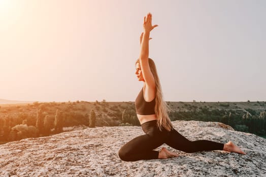 Well looking middle aged woman with long hair, fitness instructor in leggings and tops doing stretching and pilates on the rock near forest. Female fitness yoga routine concept. Healthy lifestyle.