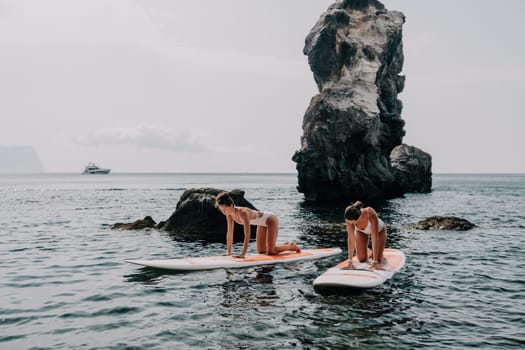 Woman sup yoga. Middle age sporty woman practising yoga pilates on paddle sup surfboard. Female stretching doing workout on sea water. Modern individual hipster outdoor summer sport activity