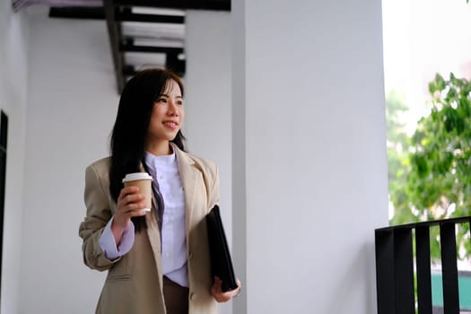 Elegant businesswoman with disposable paper coffee cup walking outside modern office building.