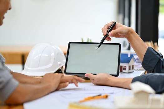 Cropped shot of Architect man pointing at digital tablet screen, discussing home renovation idea with senior female client..