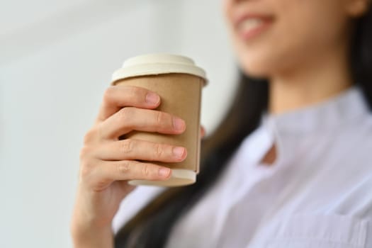 Select focus on businesswoman hand holding disposable paper coffee cup, relaxing during break.