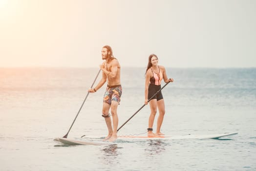 Sea woman and man on sup. Silhouette of happy young woman and man, surfing on SUP board, confident paddling through water surface. Idyllic sunset. Active lifestyle at sea or river
