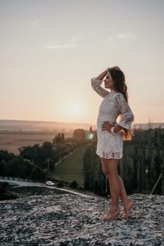 Romantic beautiful bride in white dress posing with sea and mountains in background. Stylish bride standing back on beautiful landscape of sea and mountains on sunset