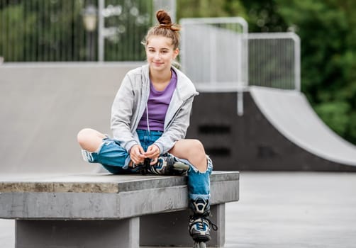 Cute girl roller skater sitting in city park and smiling. Pretty female teenager posing during rollerskating