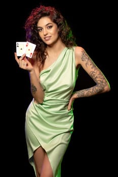 Portrait of stylish elegant young brown-haired girl happy with successful poker game standing against black background, demonstrating set of winning cards from pair of aces