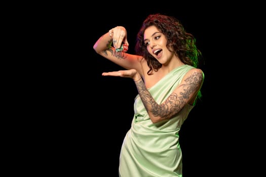 Gambling excited young brunette with tattoos on arms standing against black background, laughing while holding stack of betting chips in hands, cropped shot