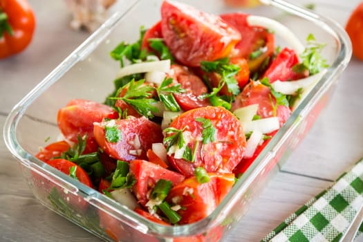 Spicy snack tomatoes with garlic, herbs, seasonings and onions in a glass bowl on a wooden table.