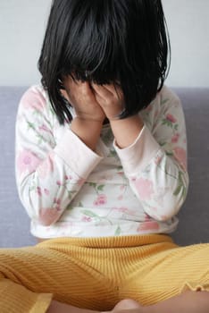 a upset child girl cover her face with hand .