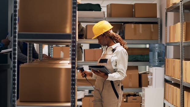 African american woman scanning barcodes on boxes, using digital tablet and scanner to ship manufacturing goods. Female supervisor working with warehouse products on depot shelves. Tripod shot.