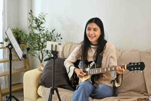 Young female musician playing electric guitar while recording a video for her social media channel.