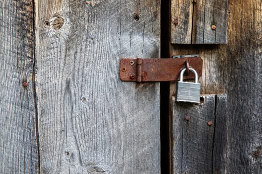Close-up of a rustic wooden door featuring a rusty padlock, emphasizing security and rustic vintage design elements. The texture highlights aged wood and metal.