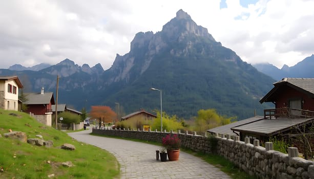 A beautiful landscape photo of a stone road winding through a village nestled in the Pyrenees Mountains. The photo captures the traditional architecture of the region, with charming stone houses and a dramatic backdrop of towering peaks. The lush green vegetation adds to the serene and picturesque scene. This image is perfect for projects related to travel, nature, architecture, and the beauty of the Pyrenees Mountains.