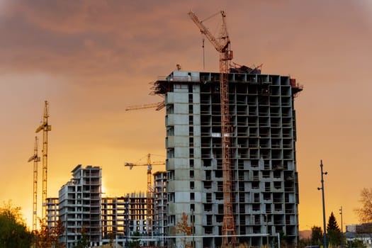 Golden sunset behind a bustling construction site with cranes and buildings silhouetted against the vibrant sky