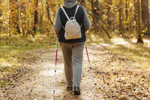 Autumn unfolds its vibrant palette, a dedicated individual engages in Nordic walking along a tranquil forest path