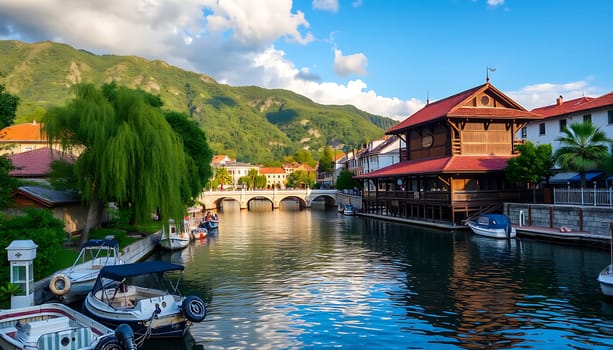 A tranquil canal winds through a charming village nestled at the foot of a mountain range. The water reflects the clear blue sky and fluffy white clouds above, creating a picturesque scene. Several boats are docked along the canal, adding to the idyllic charm of the location. The image captures the beauty of nature and architecture in perfect harmony, making it ideal for travel brochures, tourism websites, or any project related to relaxation and serene landscapes.,