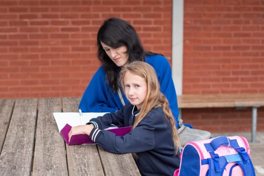 mother helping daughter with homework at wooden table in children playground doing homework, education concept, back to school,