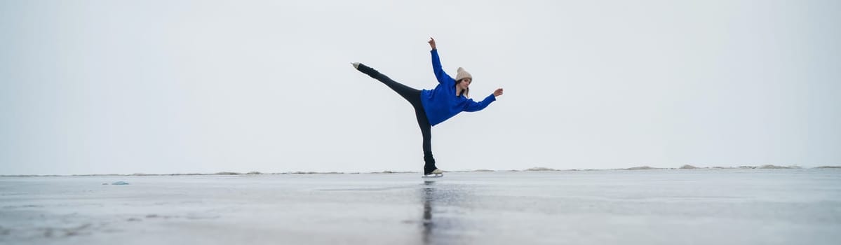 Caucasian woman in a blue sweater is skating on a frozen lake. Figure skater performs a swallow