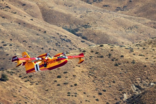 A vibrant yellow firefighting aircraft flies over dry hills, ready to combat the 2024 Valley Fire near Boise, Idaho. The plane is equipped to drop water and protect nature from devastating fires.