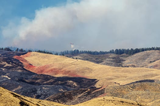 Dramatic aerial scene showing firefighting efforts over a mountainous region with visible fire lines, smoke, and charred landscapes from the 2024 Valley Fire near Boise Idaho