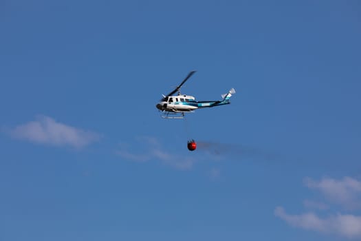 A helicopter carries a water bucket in flight, demonstrating aerial firefighting techniques. Captured against a clear blue sky while fighting the 2024 Valley Fire near Boise Idaho