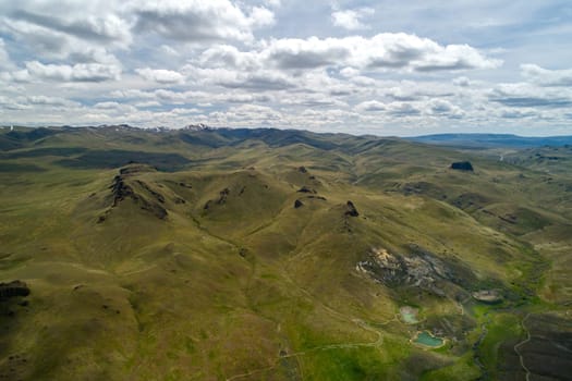 A picturesque aerial shot capturing rolling green hills under a partly cloudy sky. The vast landscape exudes tranquility and natural beauty, perfect for concepts of freedom and exploration.
