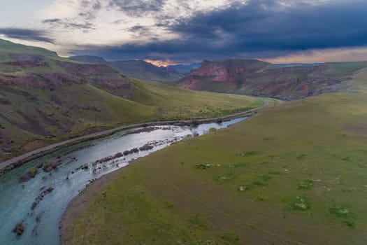 A breathtaking aerial view of a tranquil river winding through a wide, expansive valley surrounded by rolling hills and dramatic skies in Idaho