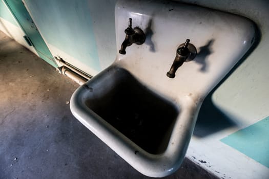 An aged ceramic basin with vintage double taps in a neglected, abandoned space. The image captures the rustic and weathered look of the surroundings, evoking feelings of nostalgia and decay.