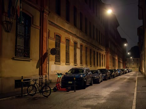 Cremona, Lombardy, Italy October 15th 2024 Electric scooters and cars parked on a deserted street in turin, italy, illuminated by streetlights at night