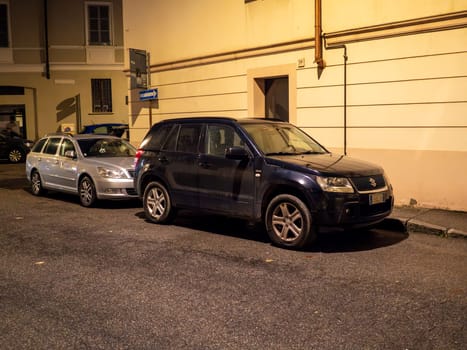Cremona, Lombardy, Italy October 15th 2024 Two cars parked on a narrow street at night, illuminating the building facades and creating a peaceful urban scene