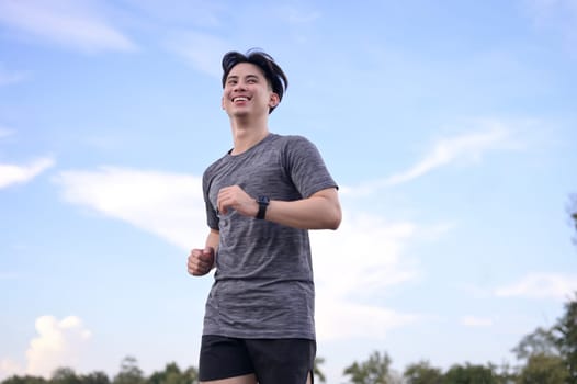 Happy smiling man jogging through a park during the late afternoon.