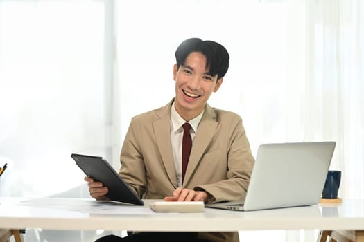 Cheerful young entrepreneur in formal suit working in modern workspace.