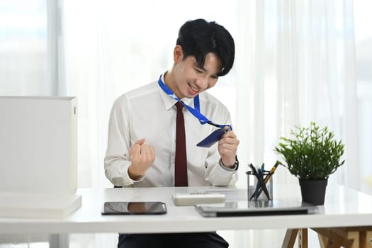 Cheerful office worker celebrating new job with ID badge in hand.