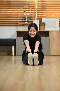 Flexible teenager girl doing stretching exercises on floor in living room.