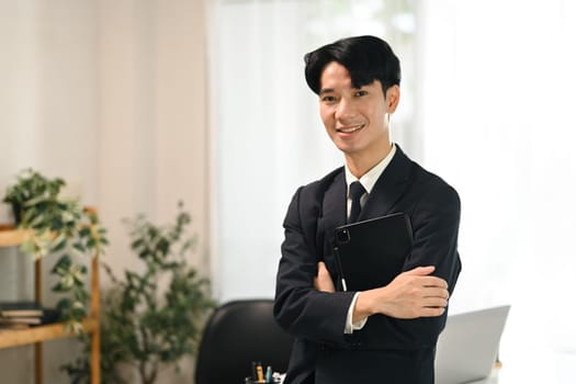 Portrait of young businessman in a suit holding a digital tablet standing in office.
