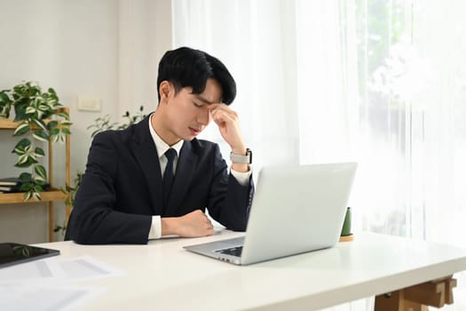 Frustrated young businessman in a business suit holding his head in hands sitting at desk.