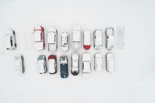 Aerial shot of parked cars covered in a thick layer of snow, showcasing winter's serene and chilly beauty. Captures the contrast of vehicles against the snowy landscape.