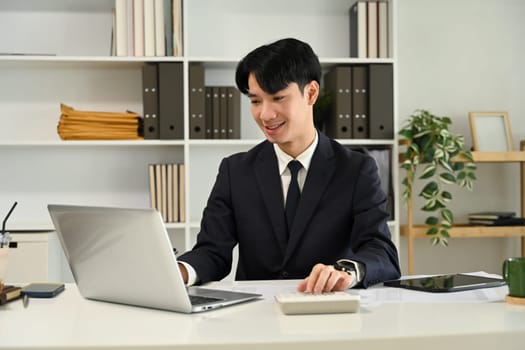 Smiling young businessman working with laptop at office.