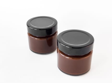 Two glass jars of chocolate spread on white background.