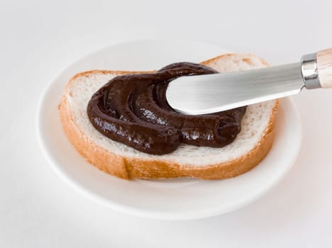 Creamy chocolate spread on fresh bread with a butter knife on a white plate.