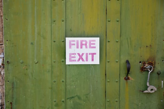 An abandoned building with a green door and a faded fire exit sign on it
